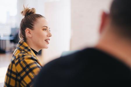 Woman with hair tied in a bun and a checked shirt sitting next to work colleague