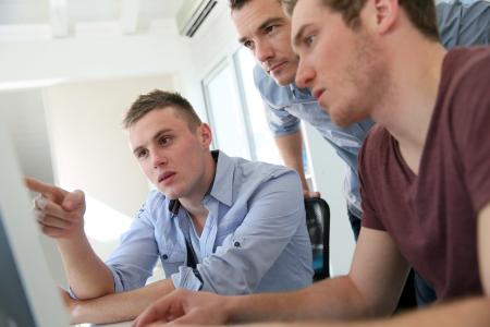 Three men working in front of a computer screen in a training session