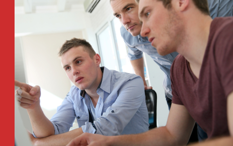 Three young male work colleagues looking at computer screen during training session