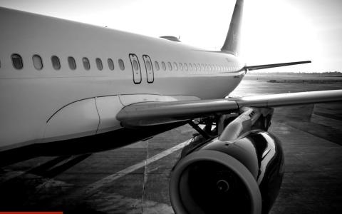 Passenger aircraft on the airport apron, showing the wing and engine, in black and white.