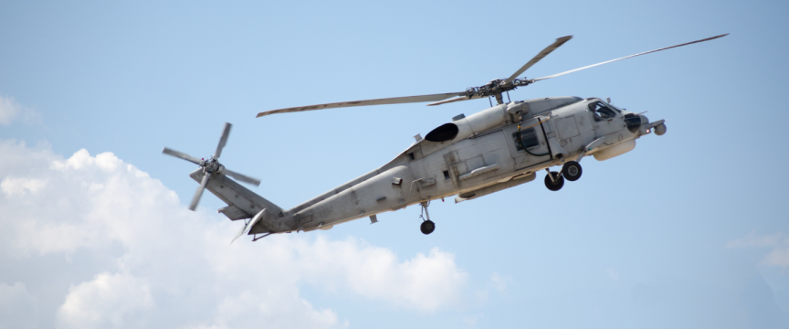 Image shows a helicopter in the air set against blue sky and light clouds