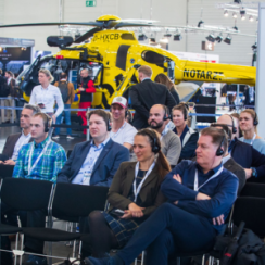 Attendees at European Rotors event with yellow helicopter on display behind