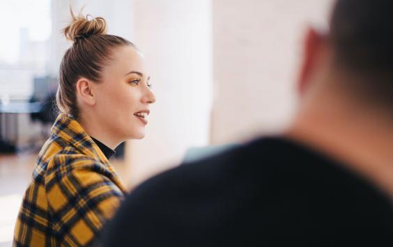 Woman with hair tied in a bun and a checked shirt sitting next to work colleague