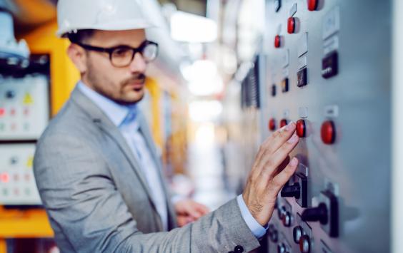 Man in grey suit and hard hat stood in front of control panel in power plant