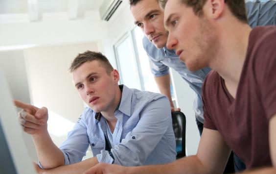 Three men working in front of a computer screen in a training session