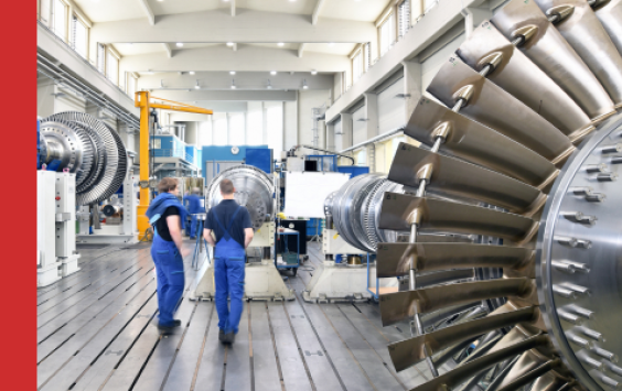 Shows back of two engineers walking in power station next to turbine