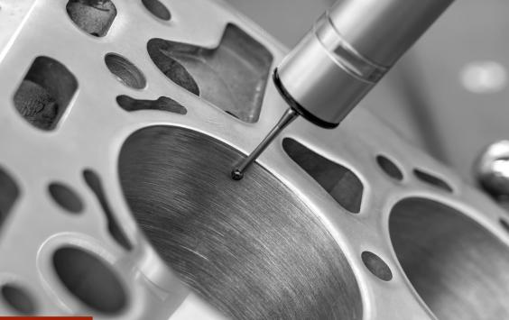 Precision measuring probe checking the surface of an engine cylinder block, in black and white.