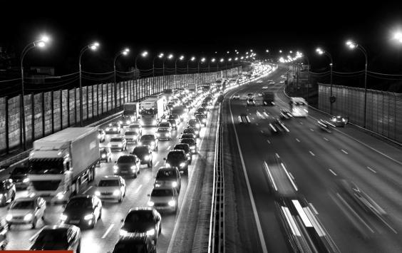 Busy motorway at night lined with noise barriers, in black and white.