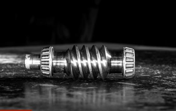 Worm gear shaft with roller bearings on a dark workshop surface, in black and white.