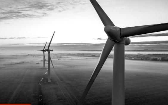Wind turbines across misty farmland at dawn, in black and white.