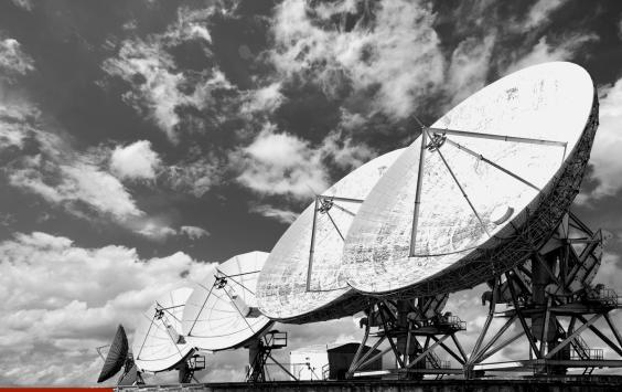 Row of large satellite dishes under a cloudy sky, in black and white.