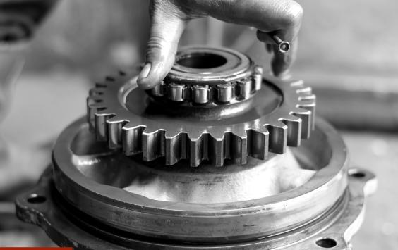 Engineer’s hand fitting a bearing into a gear assembly, in black and white.